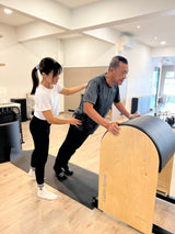 A man and woman performing a pilates exercise together in a gym setting, focusing on their form and balance.
